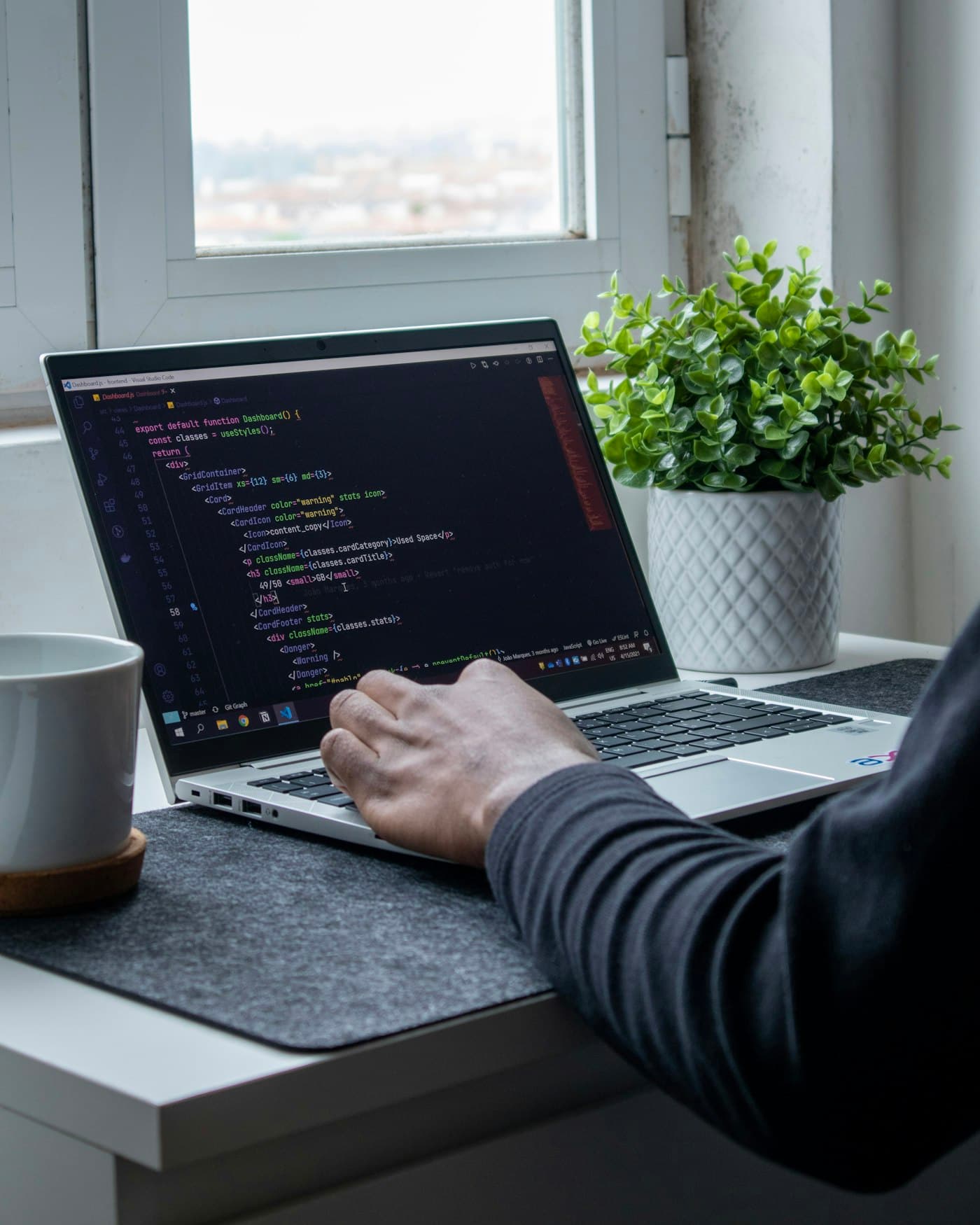 A developer working on a laptop with a plant and a mug on the desk